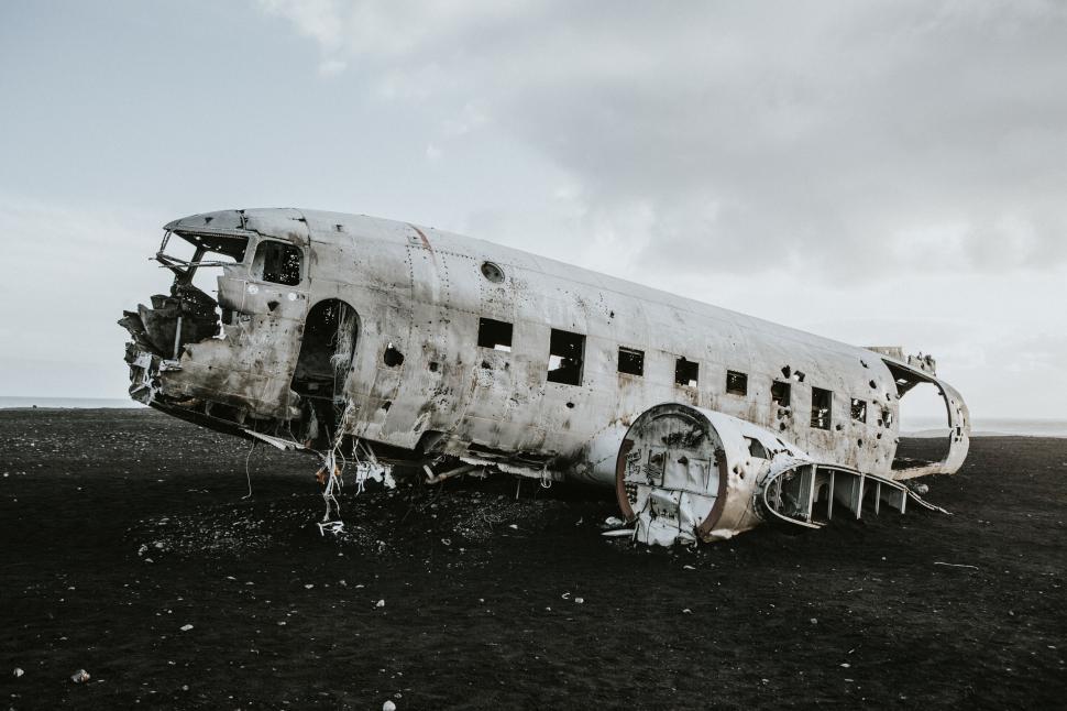 Free Image of Crashed airplane wreck on black sand beach under cloudy skies 