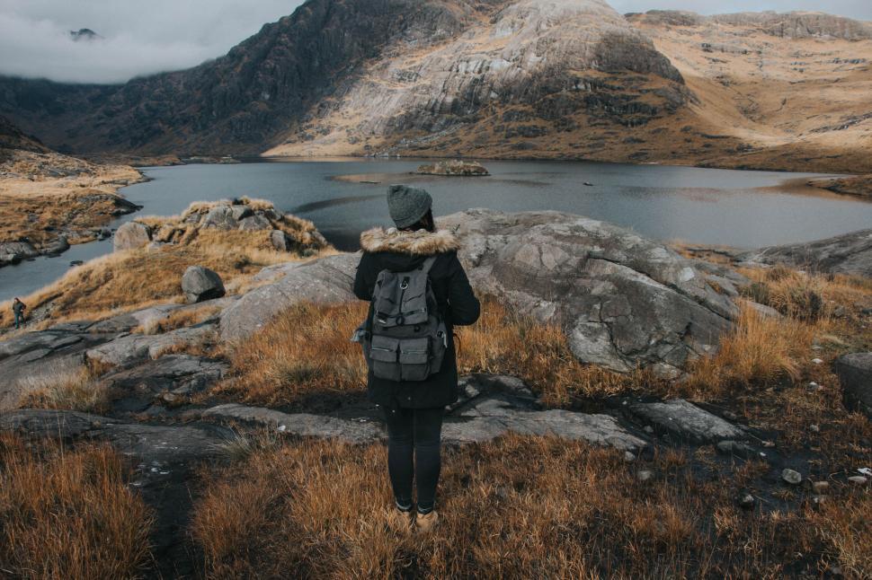 Free Image of Hiker standing in front of serene alpine lake with rocky backdrop. 