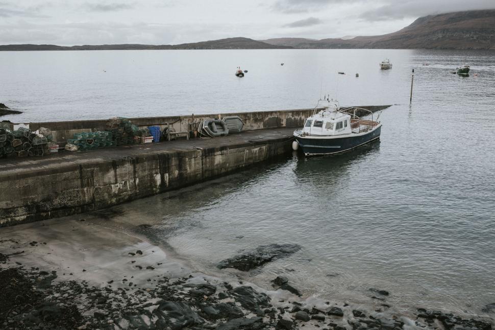 Free Image of Small fishing boat docked at pier in tranquil harbor with hills 