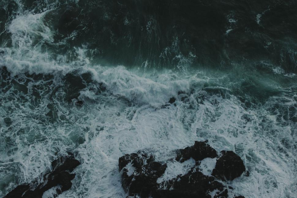 Free Image of Waves crashing on rocky shore with dark, turbulent waters foaming. 