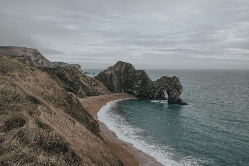Free Image of Coastal view of a stone arch in the ocean with grassy cliffs 