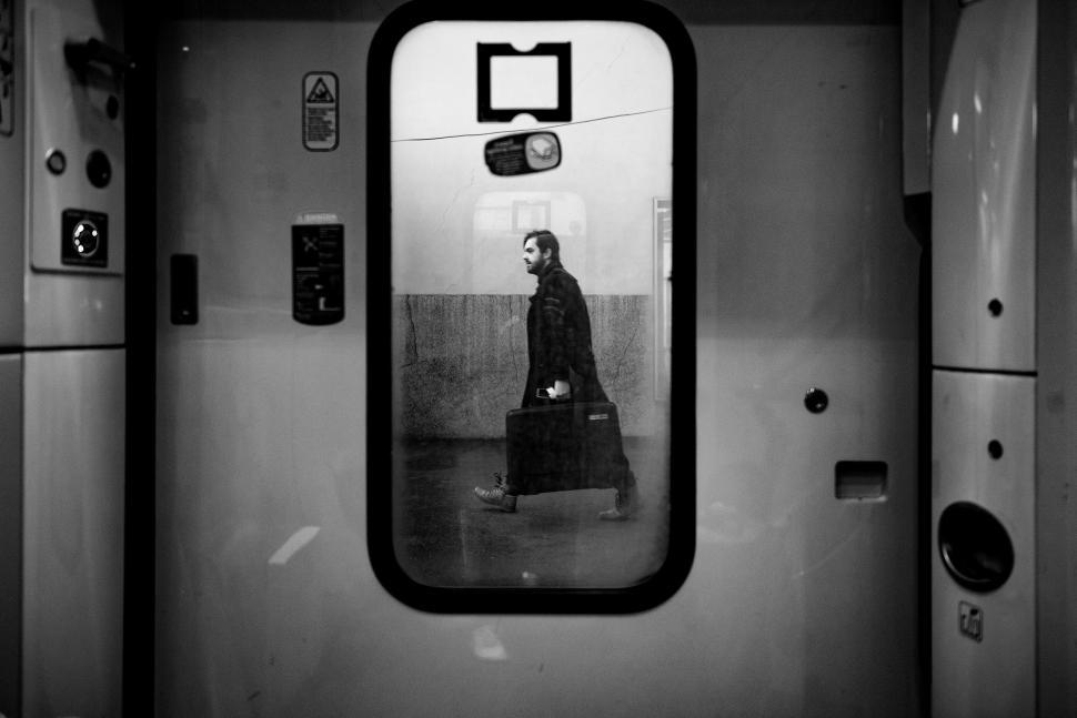 Free Image of Silhouette of a man walking with suitcase seen through subway door 