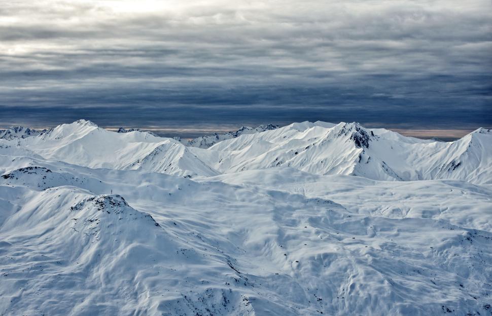 Free Image of Vast snow-covered mountain range under a dramatic cloudy sky 