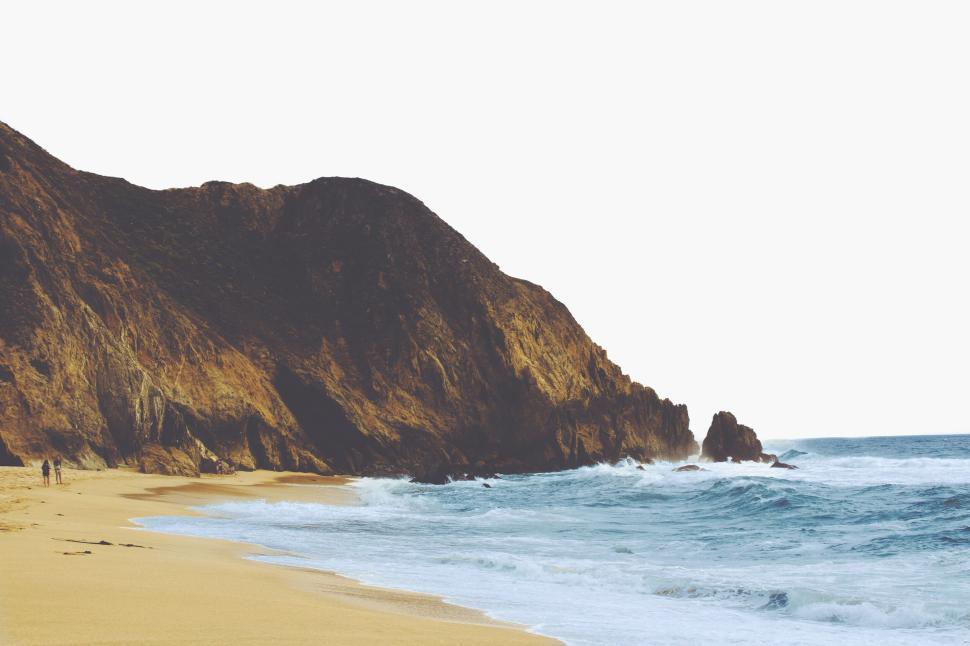 Free Image of Expansive beach with rugged cliffs and crashing ocean waves 