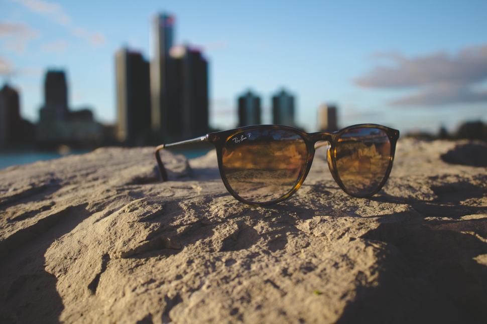 Free Image of Sunglasses on rocky surface with urban skyline background 