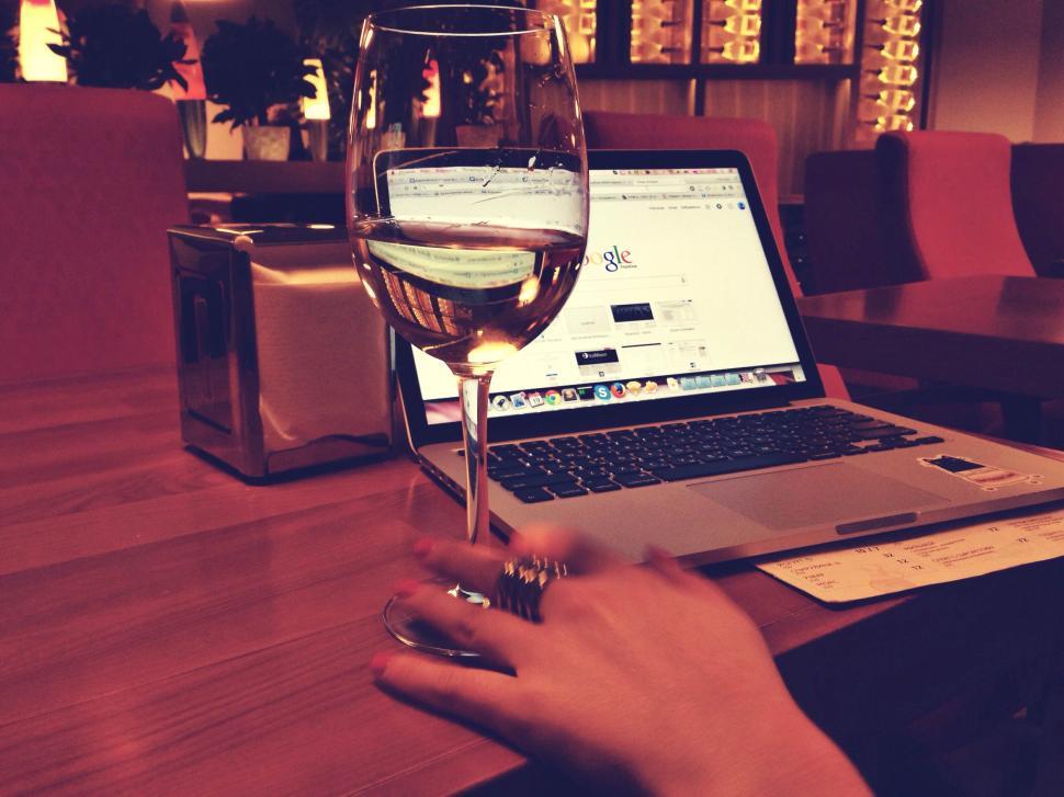 Free Image of Elegant workspace with wine glass and laptop in a dim setting 