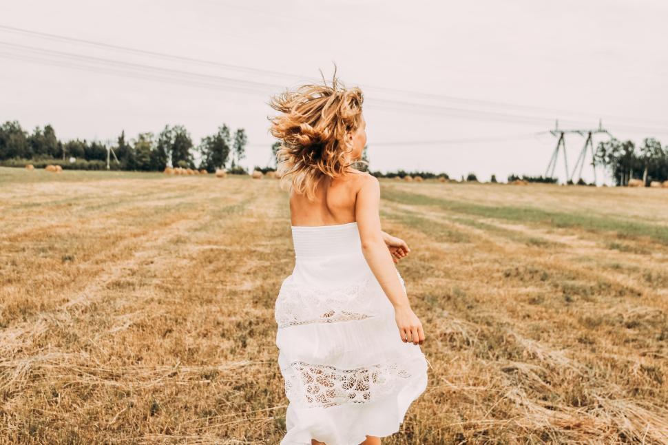 Free Image of Woman in white dress running through a dry, open field on a sunny day. 