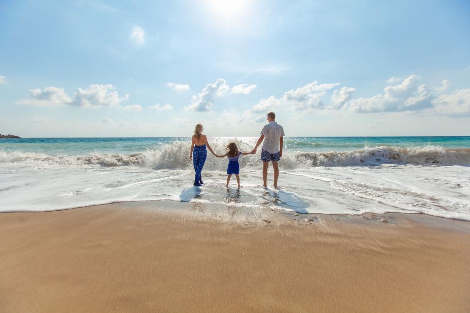 Family holding hands facing the waves on a sunny beach day.