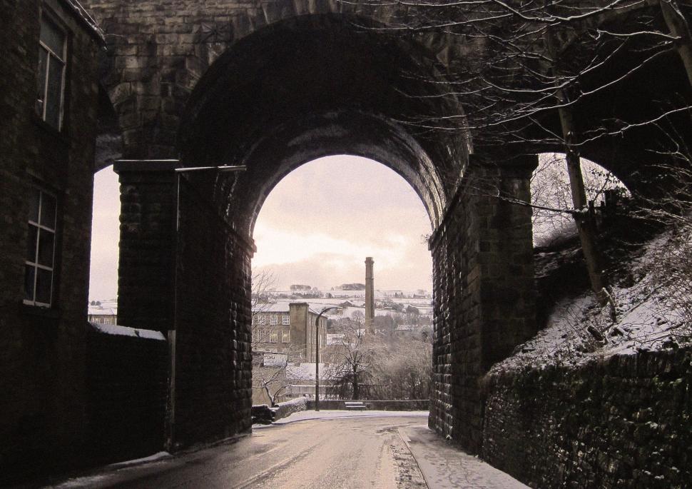 Free Image of Archway view of snow-covered town with distant chimney, winter scene 