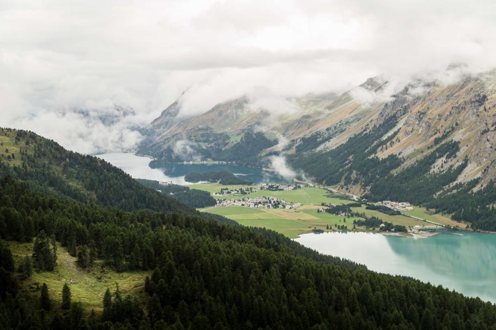 Free Image of Lush green valley with a village and lakes under cloudy skies 