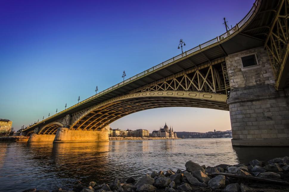 Free Image of Golden lit bridge extending over river at sunrise with city view. 
