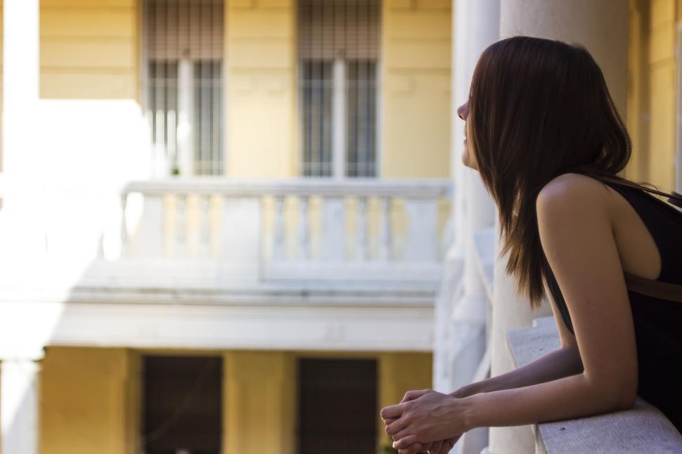 Free Image of Woman standing on balcony looking at historic building s facade 