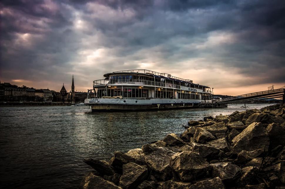Free Image of River cruise boat sailing on calm water under a dramatic sky 