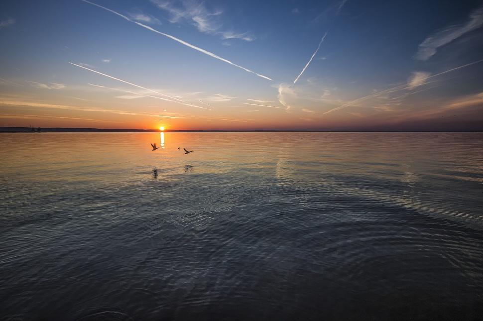Free Image of Sunset over calm lake with birds flying, tranquil and serene scene. 