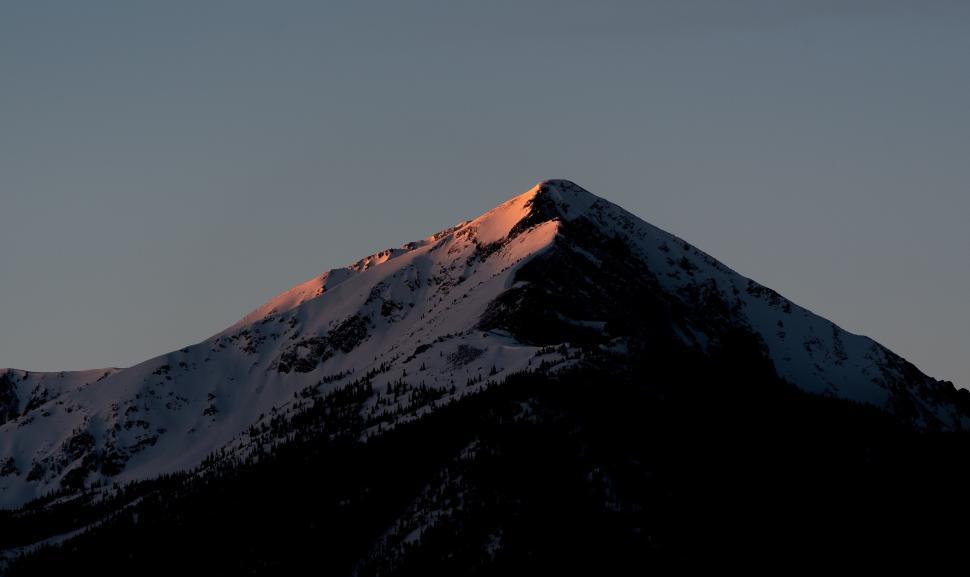 Free Image of Sunset light casts a warm glow on a snowy mountain peak. 