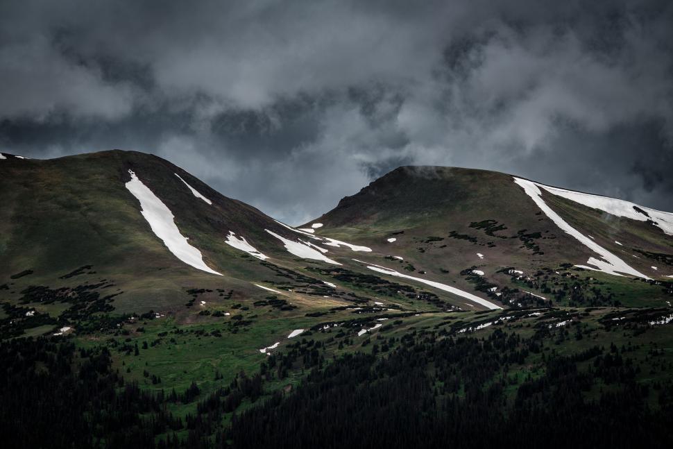 Free Image of Snow-capped mountains with patches of green under gloomy skies 