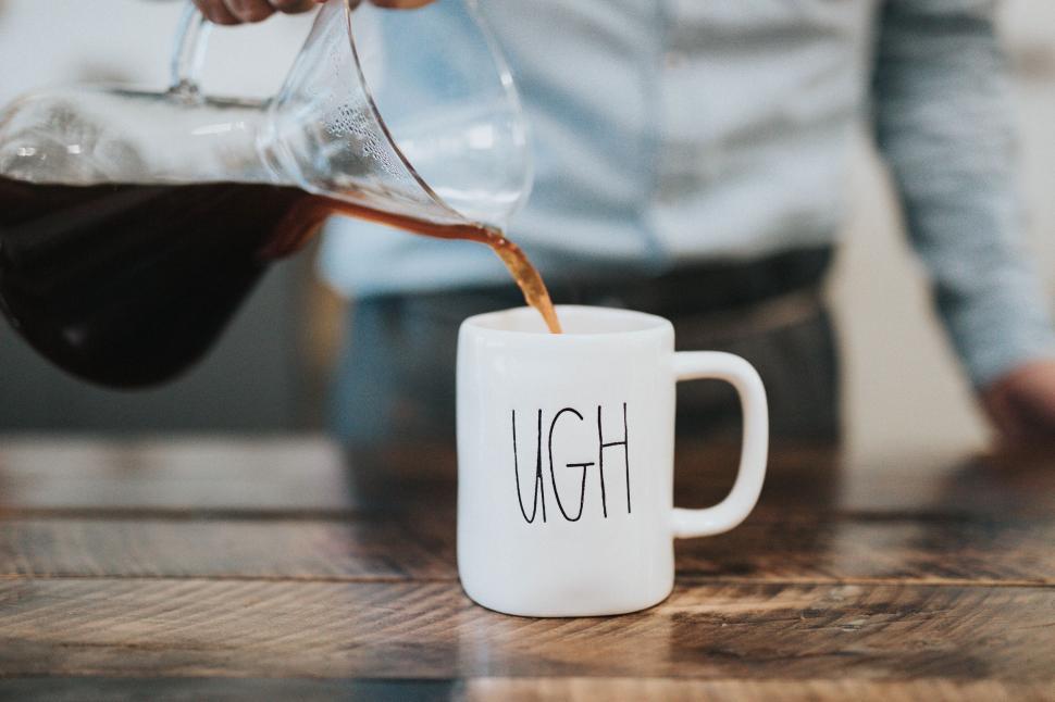 Free Image of Pouring coffee into a mug with UGH text on wooden table. 