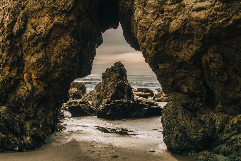 Free Image of Natural rock archway on the beach with a scenic view 