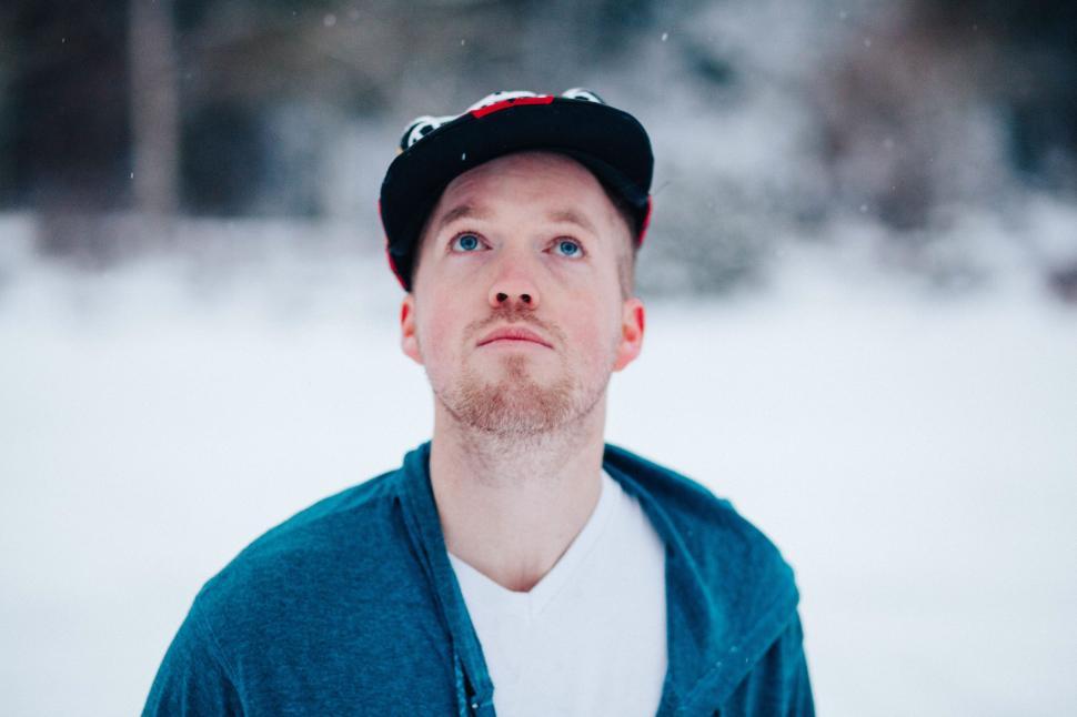Free Image of Man in blue jacket and hat looks up in snowy outdoor setting. 