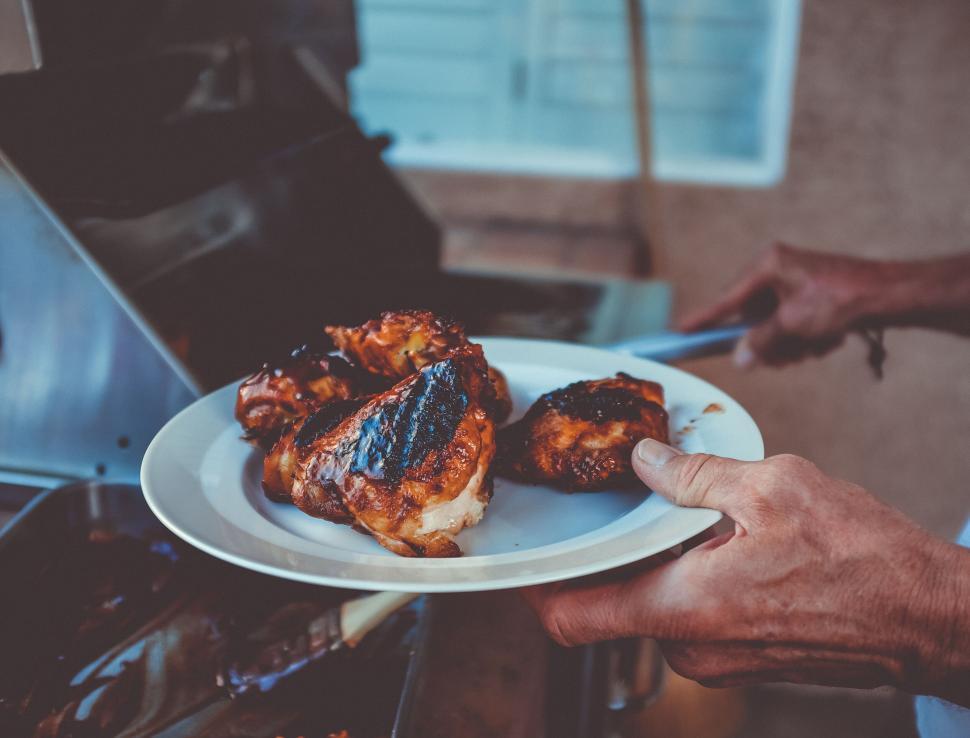 Free Image of Person holding plate with grilled meat next to grill. 