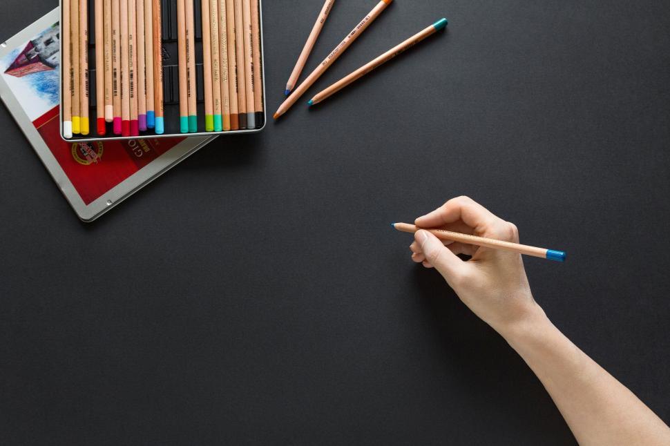Free Image of Hand holding a blue-tipped pencil on a dark background 
