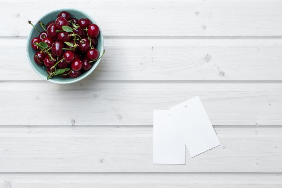 Free Image of A bowl of cherries next to two blank tags on a table 