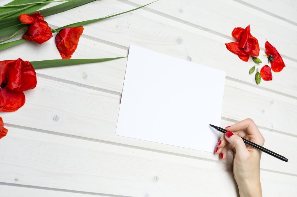 Free Image of Hand holding pen on paper with red flowers around 