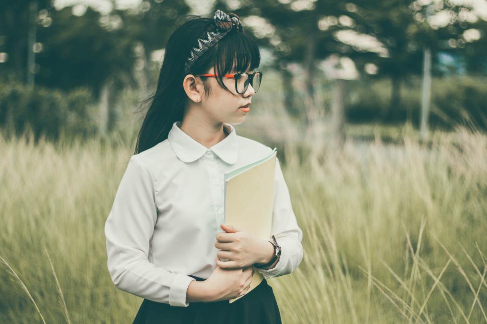 Free Image of Young woman in white blouse holding books in field 