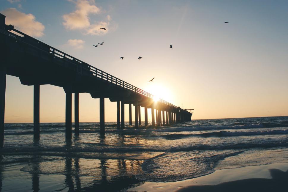 Free Image of Seaside pier at sunset with birds flying above the waters. 