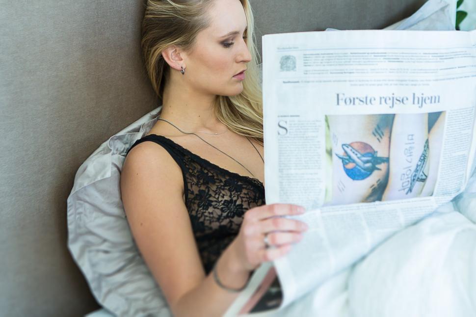 Free Image of Woman reads newspaper in bed with lace lingerie on. 