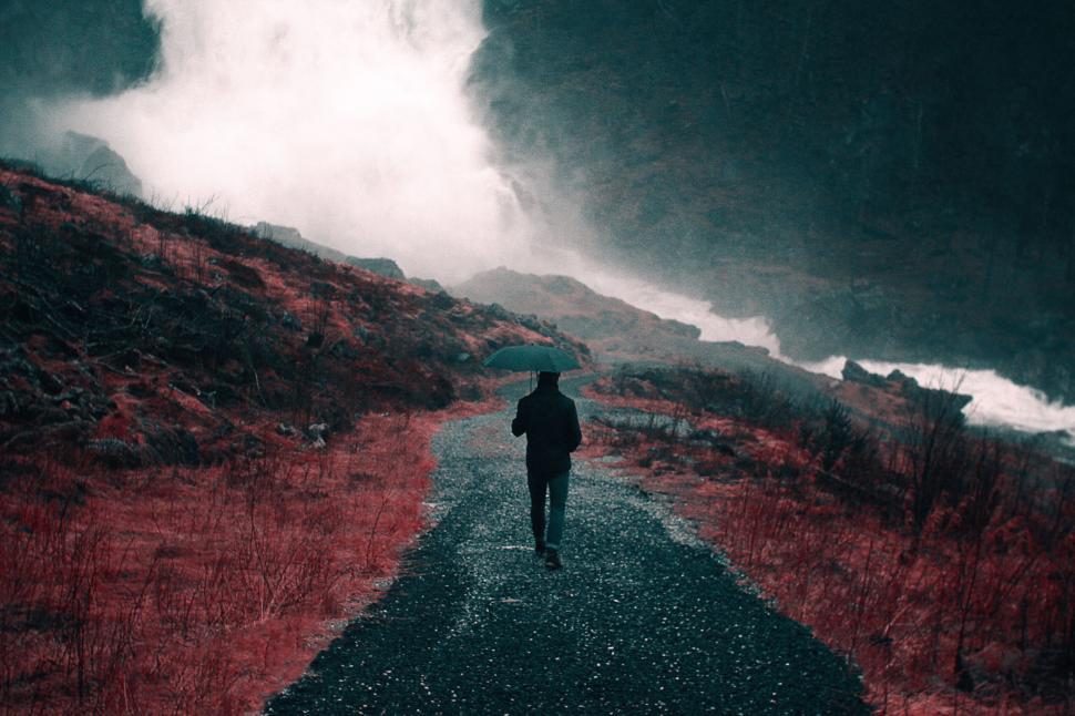 Free Image of A lone person with umbrella walking on a misty path. 