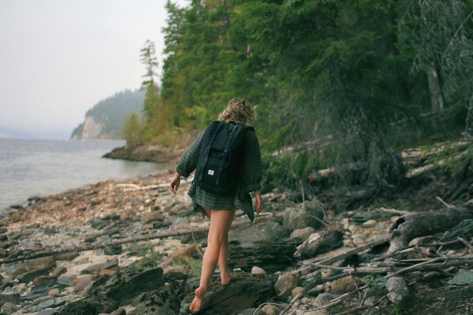 Free Image of Person hiking along a rocky lakeshore path in the forest. 