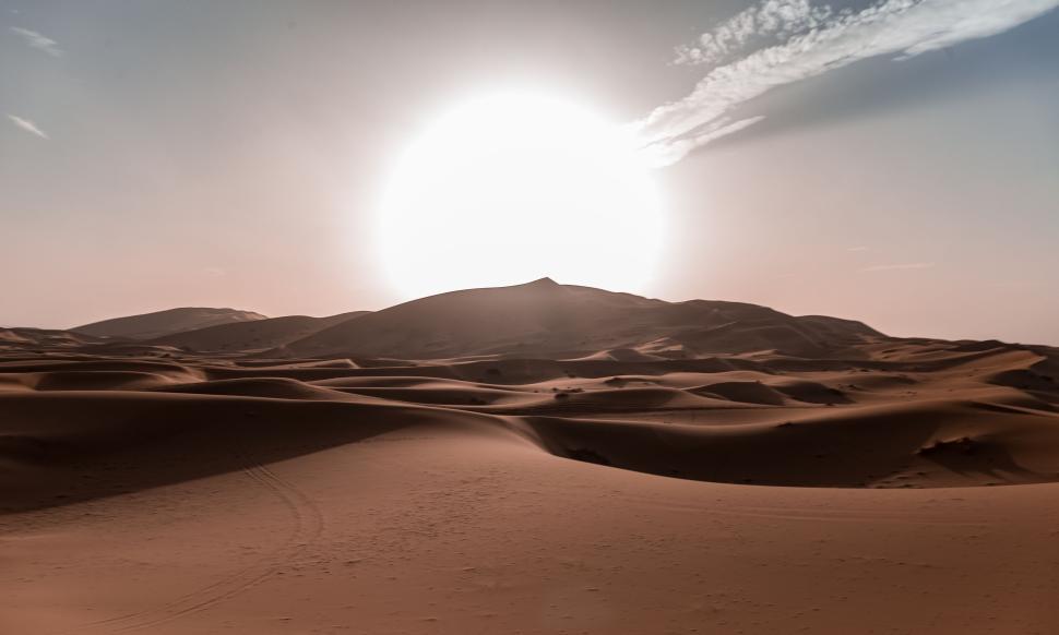 Free Image of Bright sun setting behind vast and serene desert dunes 