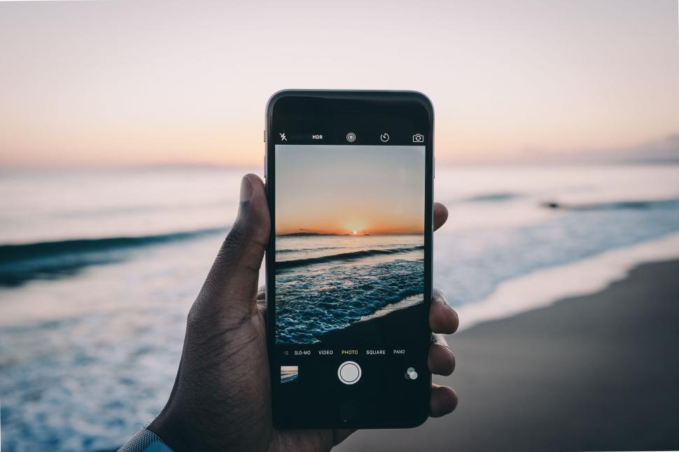 Free Image of Hand holding smartphone capturing a beach sunset 