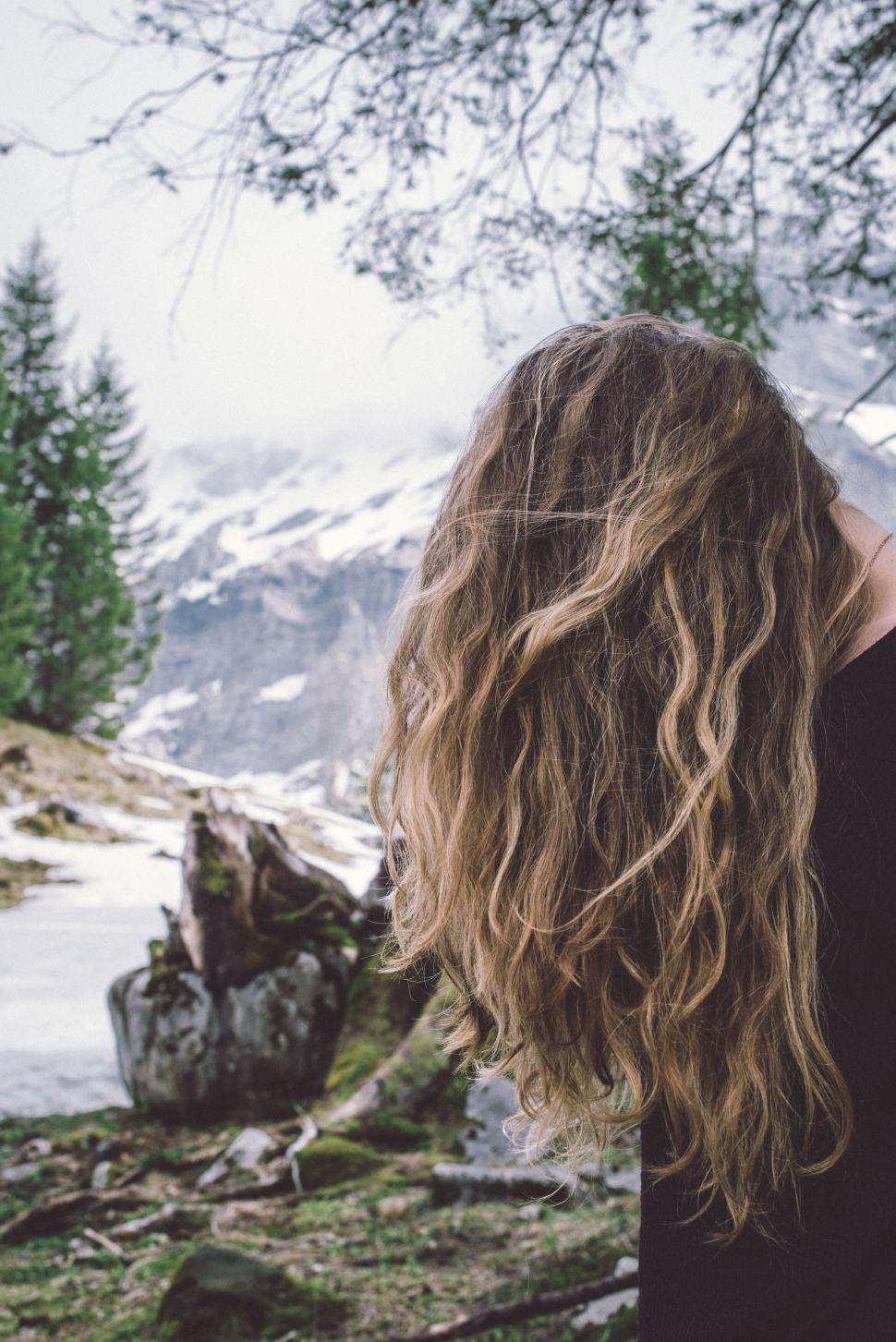 Free Image of Woman with long wavy hair standing in front of mountains. 