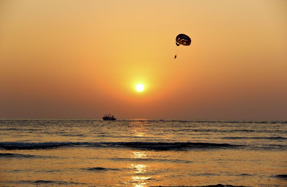 Free Image of Silhouette of parasailing at sunset over calm ocean. 