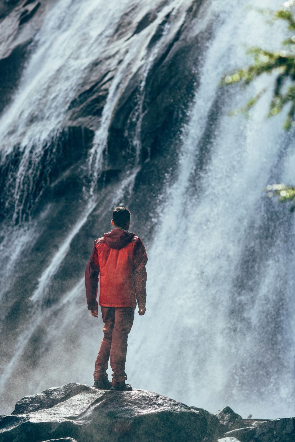 Free Image of Person in red jacket standing by a powerful waterfall. 