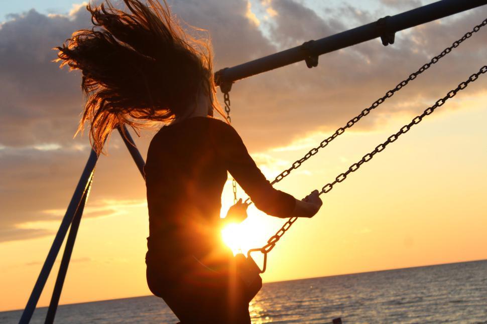 Free Image of Silhouette of a person swinging at sunset by the sea. 