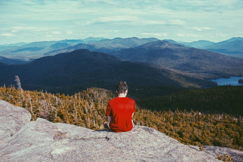 Free Image of Person in a red shirt sitting on a mountain summit. 