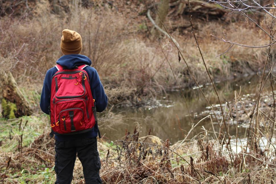 Free Image of Hiker with red backpack standing near a stream 