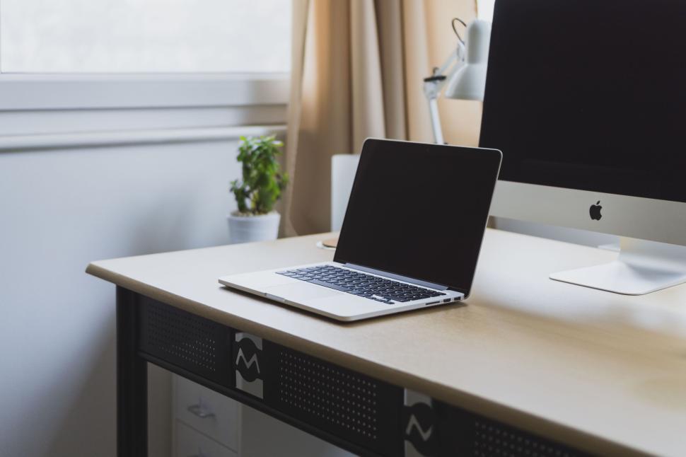 Free Image of Open laptop on a desk next to an iMac and plant. 