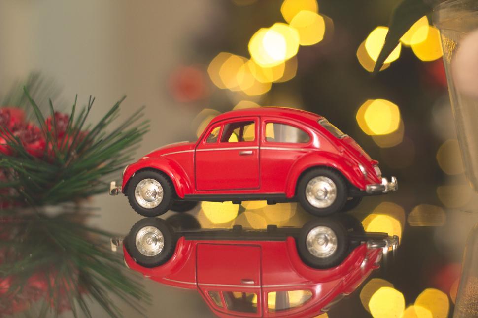 Free Image of Red toy car reflecting on a surface beside Christmas tree. 