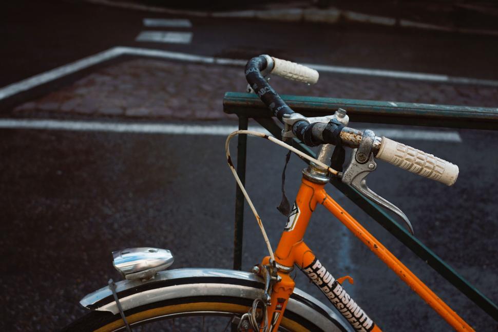 Free Image of Rusty orange bicycle parked by road rail in urban setting. 