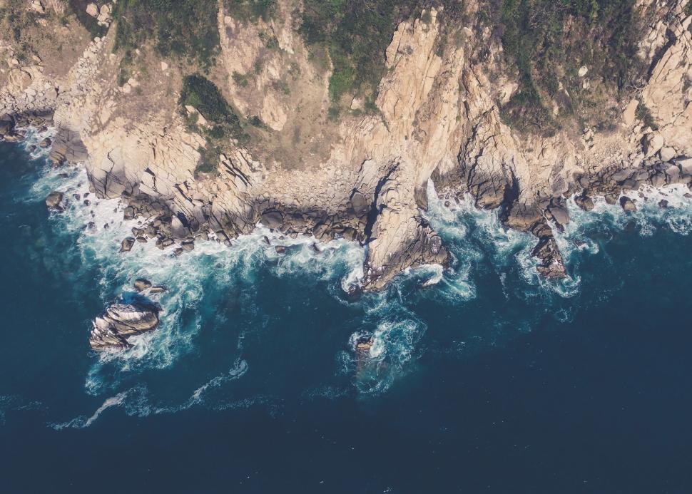 Free Image of Aerial view of rocky coastline with crashing waves 