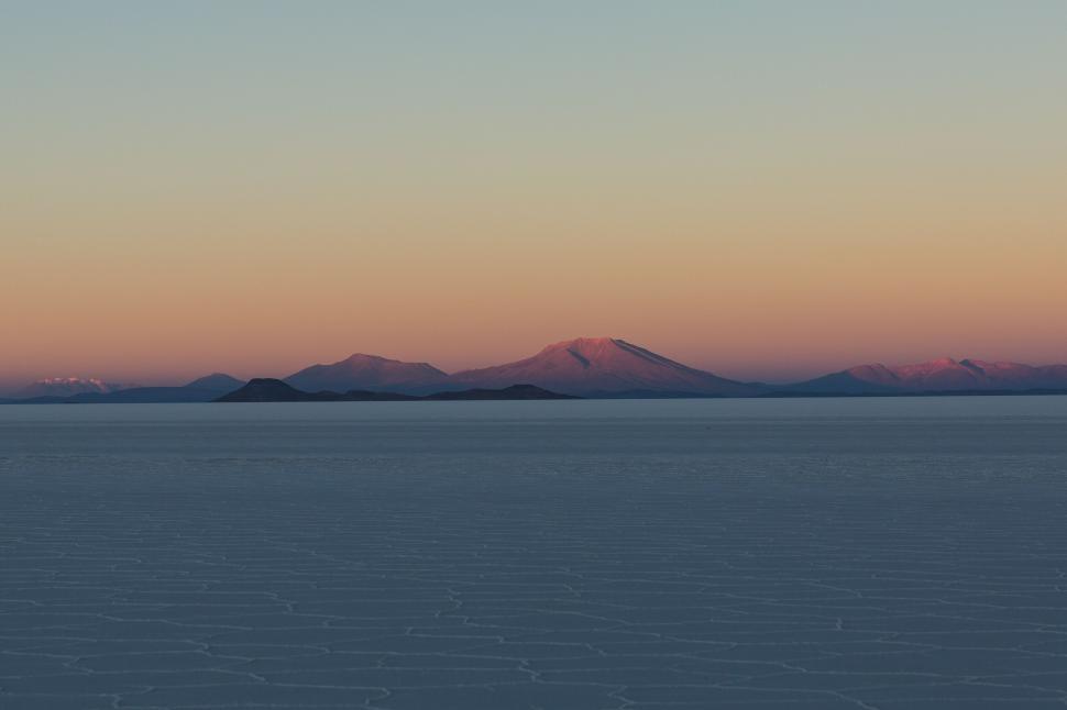 Free Image of Sunset over salt flats with distant mountains, serene 