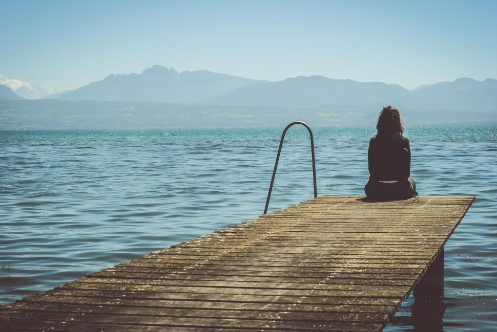 Free Image of Person sitting on dock with mountains in background. 