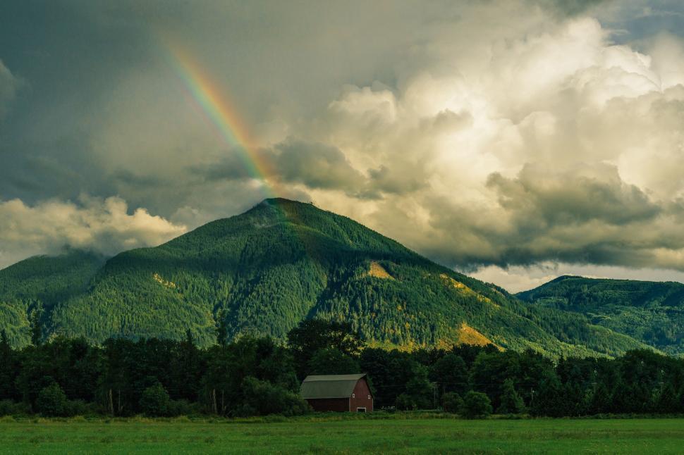 Free Image of Rainbow over green mountain with a barn beneath. 