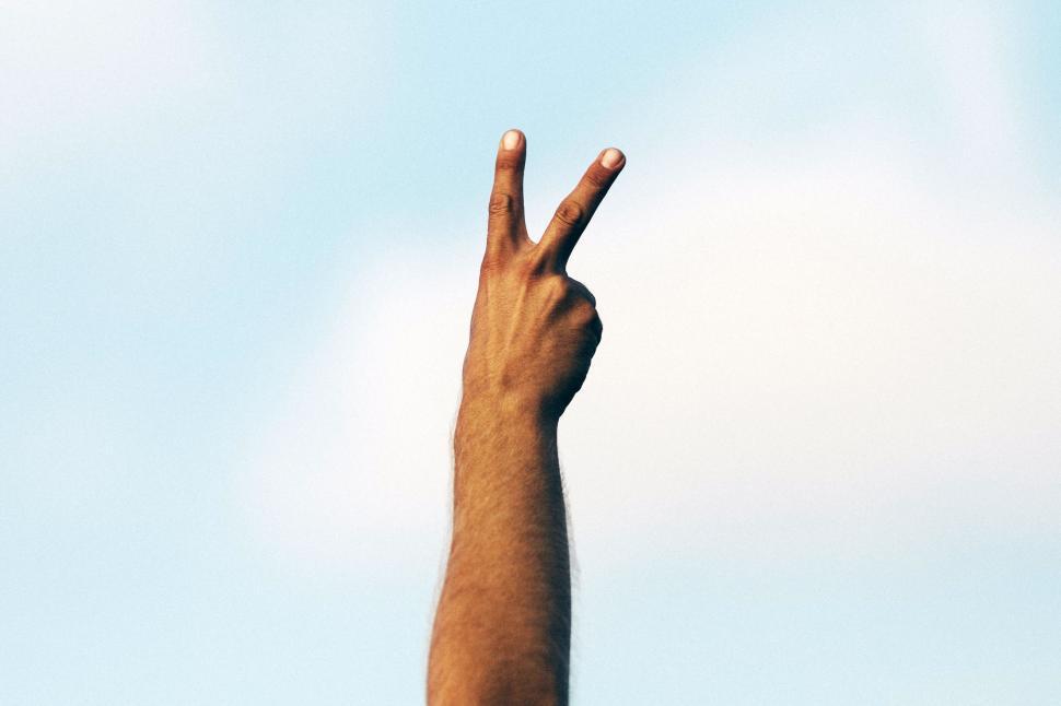 Free Image of Person making a victory sign against blue sky background 