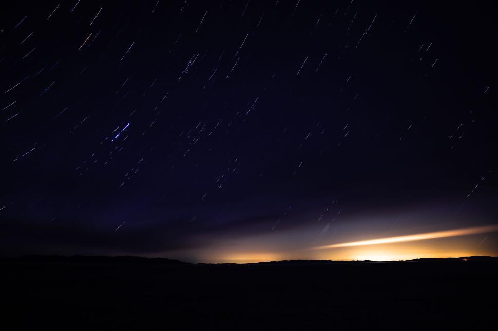 Free Image of Night sky with star trails and city lights horizon glow 