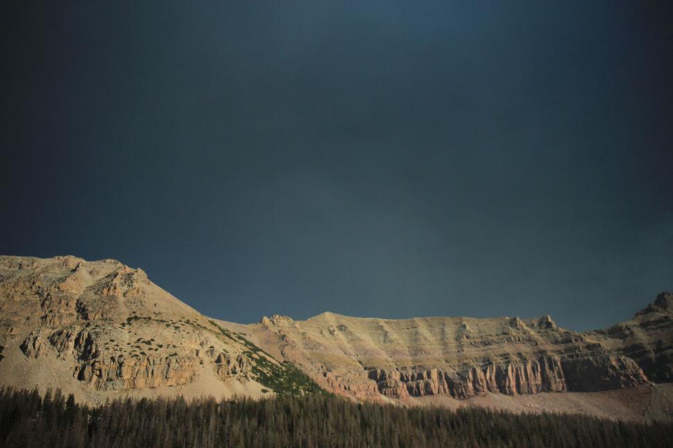 Free Image of Dramatic cliffside view with forest under a dark sky 